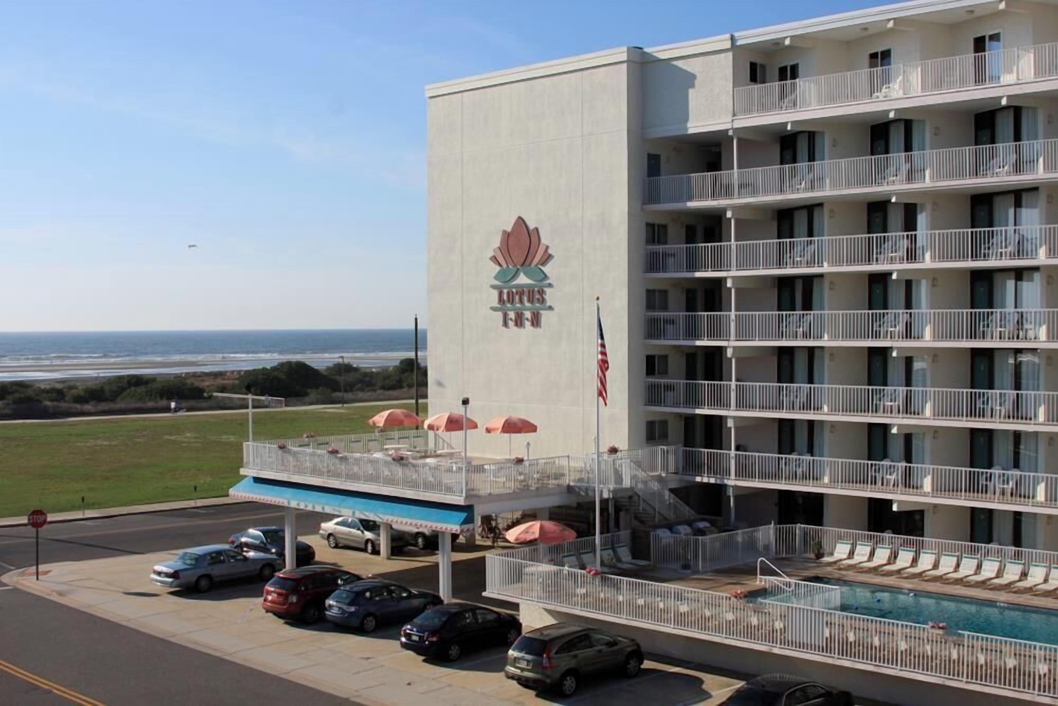 Et hotel med flere etager, hvoraf der er en swimmingpool i stueplan, et synligt amerikansk flag og udsigt til havet.