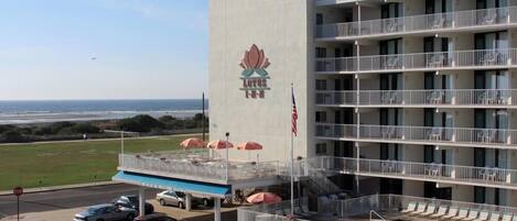 Et hotel med flere etager, hvoraf der er en swimmingpool i stueplan, et synligt amerikansk flag og udsigt til havet.