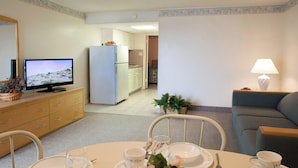 Een woonkamer met een televisie, een eettafel met borden en kopjes, een bank, en een keuken op de achtergrond.
