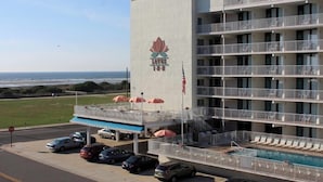 Een meerhoog hotel met een zwembad op de begane grond, een zichtbare Amerikaanse vlag en uitzicht op de oceaan.