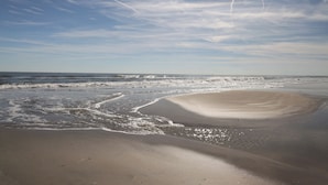 Een strand met zand, golven en een heldere lucht.