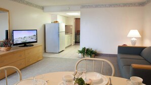 Een woonkamer met een televisie, een eettafel met borden en kopjes, een bank, en een keuken op de achtergrond.