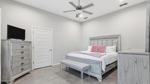 Un dormitorio con cama, banca, cómoda, televisor, ventilador de techo y puerta.