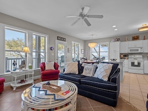 A spacious living area with a large window, a ceiling fan, and a dining area with a view. - Crabby Paddy – Ocean Club M104 (Indian Beach)