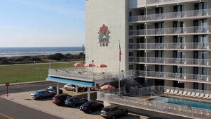 Un hotel de varios pisos con piscina en la planta baja, una bandera estadounidense visible y vista al océano.