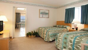 Habitación de hotel con dos camas, un escritorio con lámpara, una silla, un balcón con vistas y un cuadro en la pared.