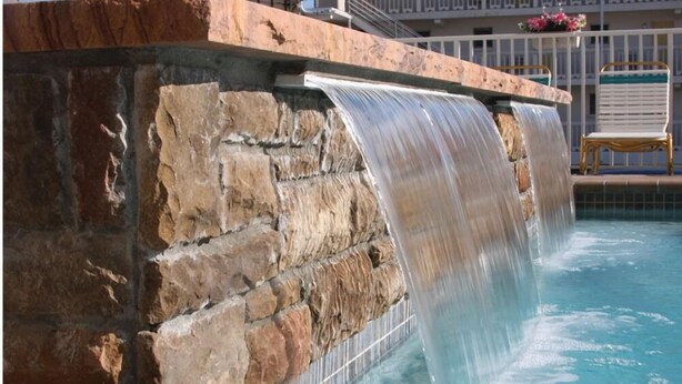 Pared de piedra con una cascada que desemboca en una piscina.