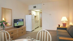 A dining area with a table set for two, a television, a refrigerator, and a sofa. - Lotus Inn - Deluxe Poolside Efficiency Suite (Wildwood Crest)
