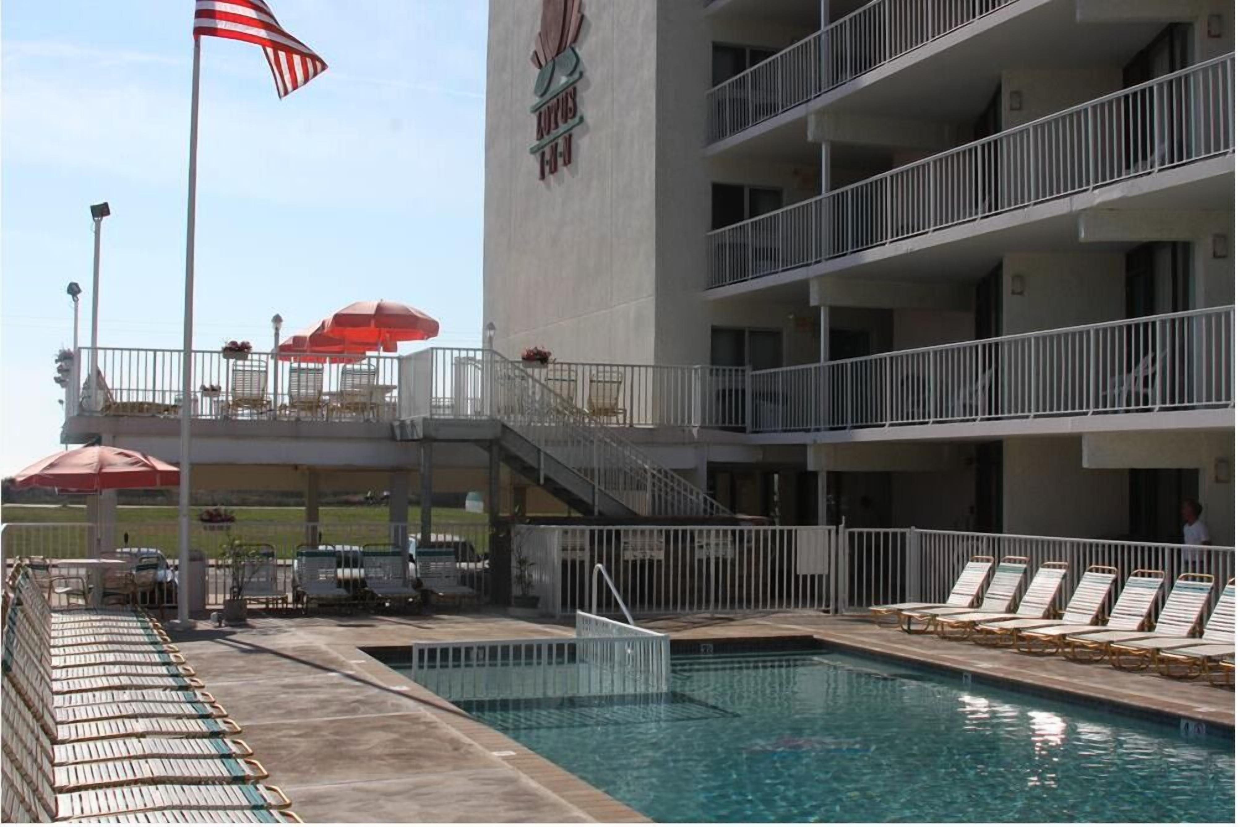 Un hotel con piscina, mobiliario exterior y una bandera.