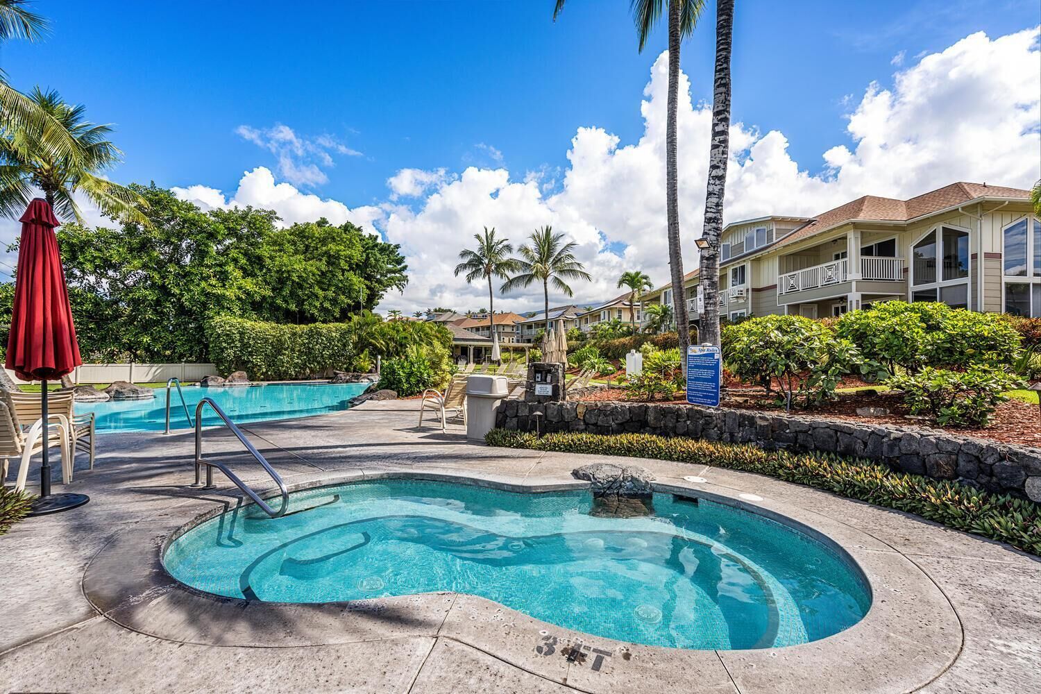 A hotel with a swimming pool, lounge chairs, and palm trees.