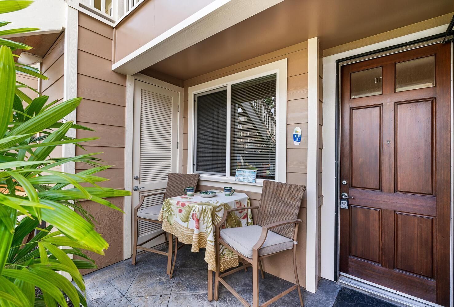 A small outdoor seating area with a table and chairs, a wooden door, and a window with blinds.