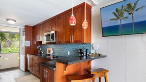 Een keuken met houten kastjes, een magnetron, een koffiezetapparaat en uitzicht op de oceaan door een raam.