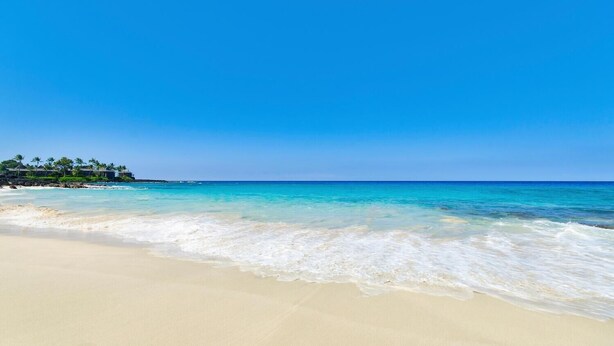 Een strand met helder turquoise water, een zandstrand en een resort met palmbomen.