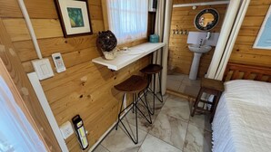 A small, wooden cabin-style room with a bed, a white sink, a small bar area with stools, and framed pictures on the wall. - Cozy 1-bedroom cabin perfect for 2 in Willemstad (Willemstad)