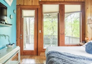 A bedroom with a bed, a nightstand, a dresser, a window with a view of a deck and trees, and a ceiling fan. - River front two bedroom cabin with a hot tub on 174 acre and plenty of wildlife (Broken Bow)