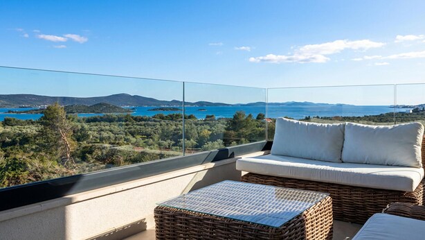 A balcony with a wicker sofa and ottoman, offering a view of a coastal landscape. - 2 bedroom awesome apartment in Turanj (Turanj)