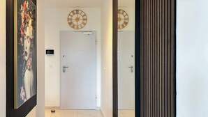 A hallway with a white door, a wall-mounted clock, a security camera, and a blue bench. - 2 bedroom awesome apartment in Turanj (Turanj)