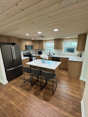 A modern kitchen with wooden cabinets, a black refrigerator, a microwave, and a dining area with a marble countertop and four chairs. - Weeki Wachee Main River • Kayaks • Private Stairs • Large Yard • Manatees (Spring Hill)
