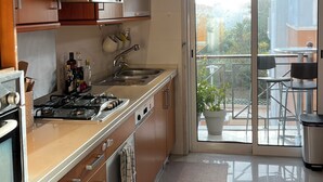 Cocina moderna con estufa a gas, horno y pileta de acero inoxidable. Cuenta con una puerta corrediza de vidrio que da a un balcón con mobiliario exterior.