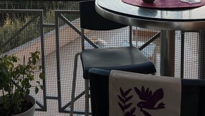 Un balcón con una mesa lista para dos personas, una silla y una planta en maceta.