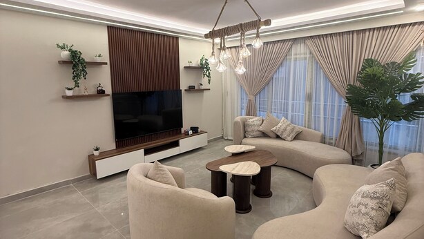 Una sala de estar moderna con un sofá curvo, un televisor de pantalla plana y una lámpara colgante original hecha de cuerda.