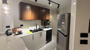 Una cocina moderna con azulejos blancos, armarios de madera, un refrigerador de acero inoxidable, un microondas y una lavadora.