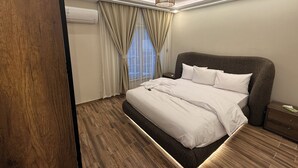 Un dormitorio moderno con una cama grande, piso de madera, una lámpara de techo y una ventana con cortinas.