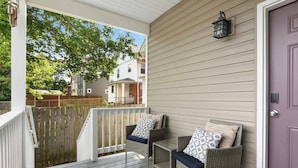 A porch with wicker chairs and a table, a wooden fence, and a purple door. - Spacious Home for 10 • Backyard • Sleeps Groups (Cincinnati)