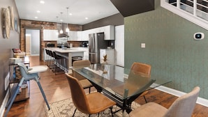 A modern kitchen with a central island, white cabinets, and a dining area with a glass table and chairs. - Spacious Home for 10 • Backyard • Sleeps Groups (Cincinnati)
