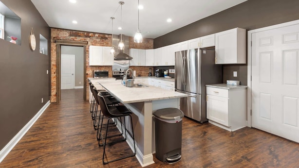 A modern kitchen with a central island, stainless steel appliances, and a brick accent wall. - Spacious Home for 10 • Backyard • Sleeps Groups (Cincinnati)