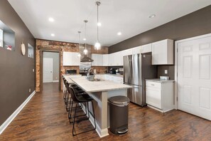 A modern kitchen with a central island, stainless steel appliances, and a brick accent wall. - Spacious Home for 10 • Backyard • Sleeps Groups (Cincinnati)