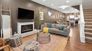 A modern living room with a fireplace, a sofa, ottomans, and a TV. - Spacious Home for 10 • Backyard • Sleeps Groups (Cincinnati)