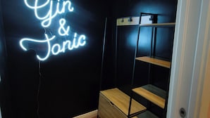Una habitación con un letrero de neón que dice 'Gin & Tonic' en la pared, suelo de madera y una estantería metálica.