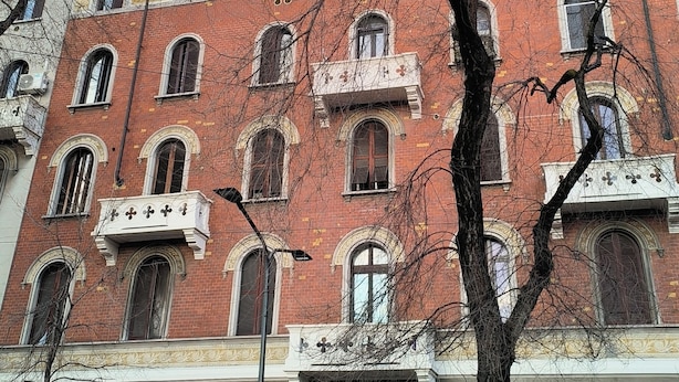Un edificio de varios pisos con fachada de ladrillo rojo, ventanas arqueadas y un balcón.