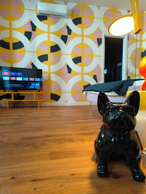 Une pièce avec un plancher en bois, une statuette de chien noir, un téléviseur affichant un écran d’accueil et un mur orné d’un motif.
