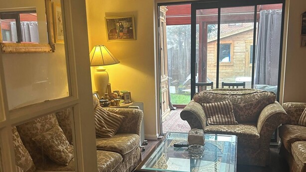 Sala de estar com mesa de centro de vidro, sofás estampados, luminária e vista para área externa através de uma porta de vidro.