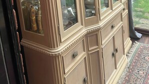 Um armário tradicional com portas de vidro, contendo diversos utensílios de cozinha e objetos decorativos.