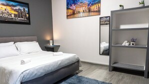 Une chambre d’hôtel moderne avec un grand lit, une table de chevet, un miroir et une étagère grise.