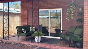 Un patio con dos sillas verdes, una planta en maceta y una puerta metálica decorativa.