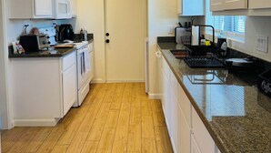 Una cocina con armarios blancos, microondas, estufa y cafetera.