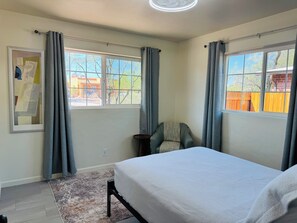 A bedroom with a bed, two windows with curtains, a chair, and a rug. - Midcentury 2-Bedroom Home Near University of Arizona (Tucson)