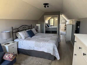A bedroom with a bed, nightstands, a dresser, a mirror, and a laundry area.