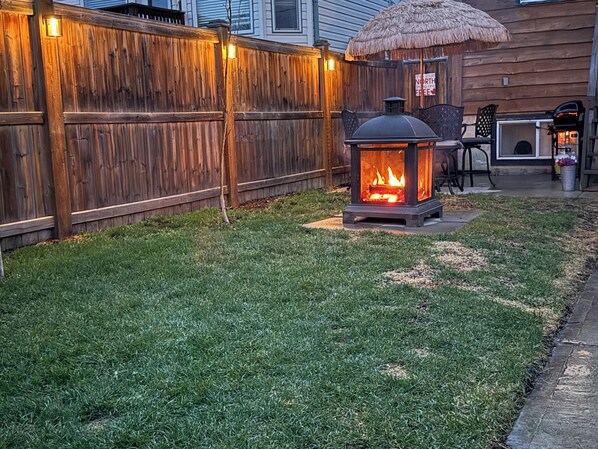A backyard with a wooden fence, a fire pit, and outdoor furniture.