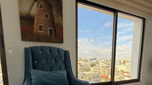 Ein smaragdgrüner Sessel in einem Zimmer mit einem großen Fenster, einem Windmühlenbild und einem Fliesenboden.