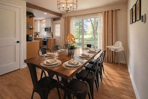 A dining area with a wooden table set for six, surrounded by black chairs, a potted plant, and a white chair.