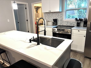 A modern kitchen with a white marble countertop, stainless steel appliances, and a window with a view of trees. - Walk to downtown Athens, relax in this stylish 2BR/2BA home near everything UGA (Athens)