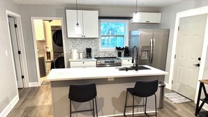 A modern kitchen with a central island, two bar stools, a refrigerator, and a window with a view.