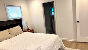 A bedroom with a bed, bedside table, lamp, and a door leading to another room.