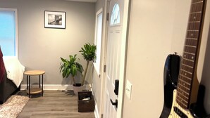 A hallway with a wooden floor, a potted plant, a framed picture on the wall, and a guitar leaning against the wall.