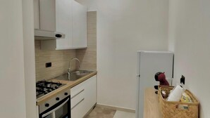A small kitchen with white cabinets, a gas stove, a sink, and a refrigerator. - B&b SunHouse (Napoli)
